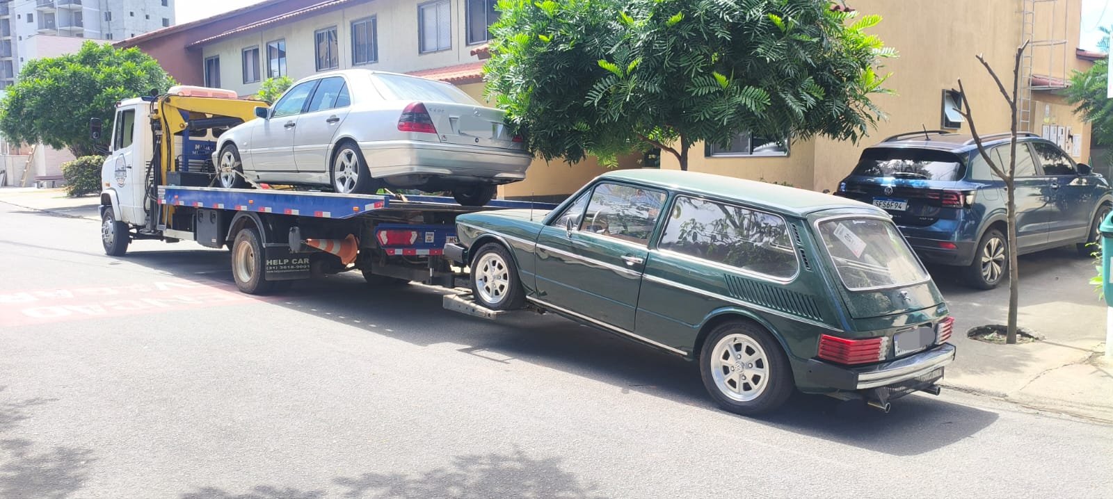 Dois carros de uma vez: um Mercedes prata na plataforma e uma Brasília verde engatada atrás.
