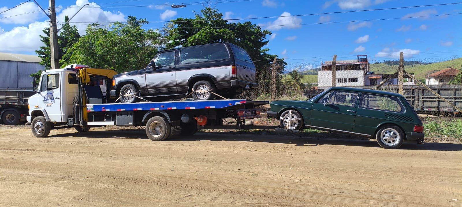 Bonanza preta na plataforma e uma Brasília verde engatada atrás, em rua de terra.